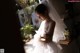 A woman in a wedding dress standing by a window.