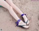 A woman is sitting on the sand with her feet in sandals.