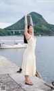 A woman in a white dress standing on a pier by the water.