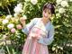 A woman in a pink and blue dress holding a flower.