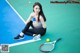 A woman sitting on a tennis court holding a tennis racket.