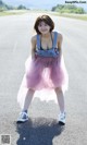 A woman in a pink tulle skirt and denim overalls posing on a road.